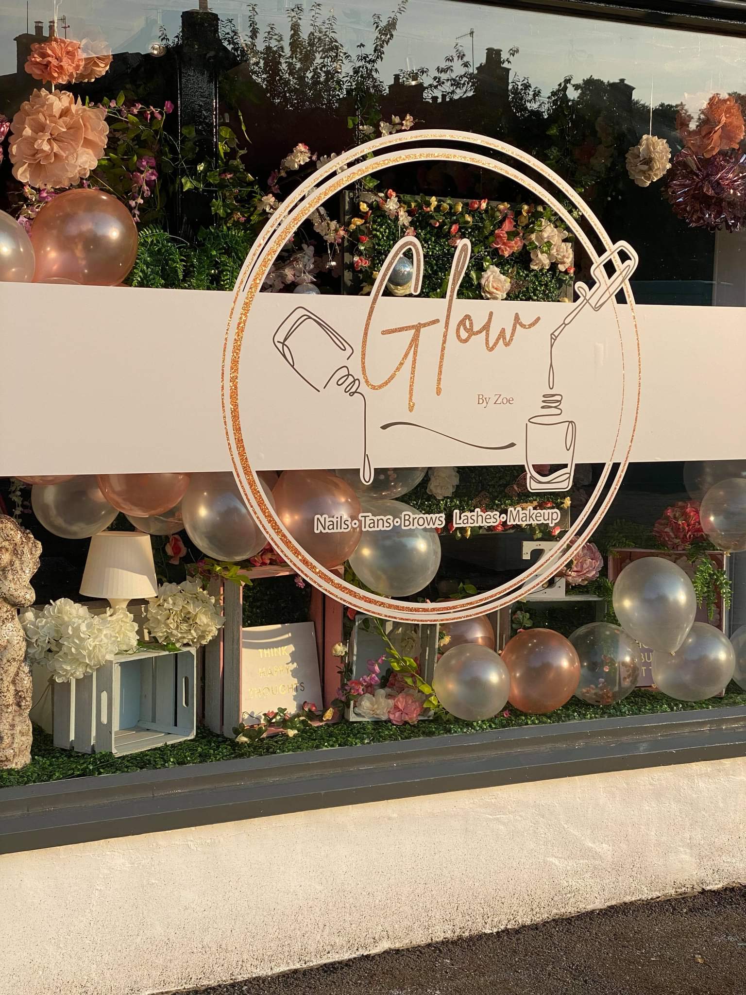 Our shop window in Bakewell with the rose gold Glow by Zoe sign, paper flowers and balloons